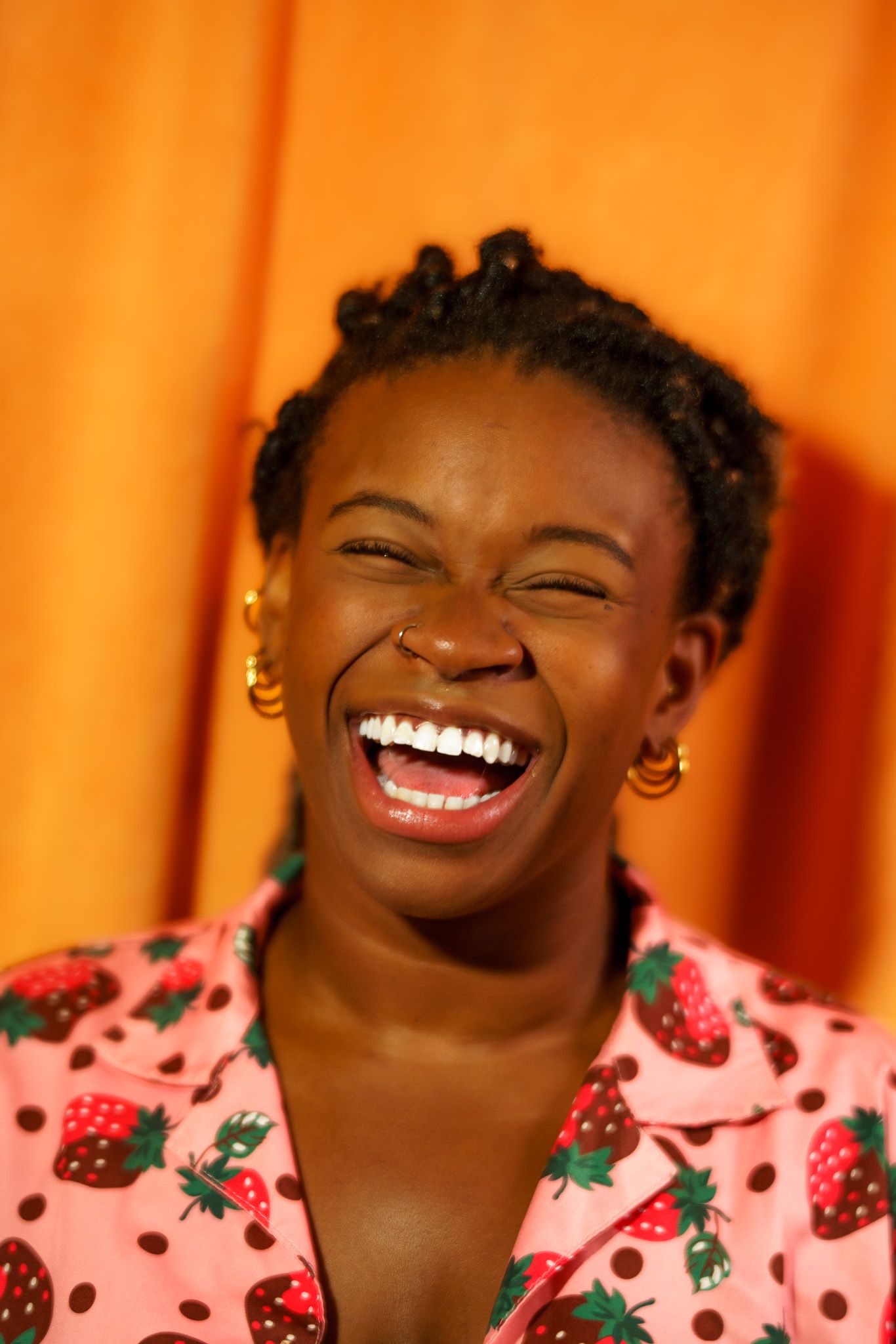Sami Beason laughing in a pink strawberry-print shirt against a warm orange backdrop